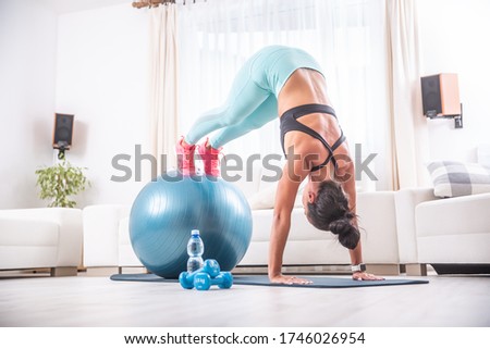 Brunette in sportswear balancing a handstand with feet on a fit ball at home  workout.