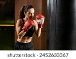 A brunette sportswoman in active wear, wearing red boxing gloves, fiercely boxing in a gym.