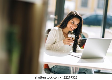 Brunette studying on laptop and enjoying coffee
