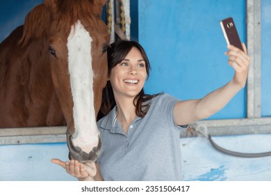 brunette taking a selfie with his horse in the stables - Powered by Shutterstock