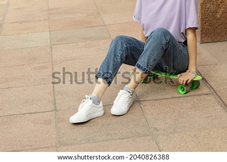 brunette teen girl with glasses with a green skateboard on the streets of the city on a clear sunny day