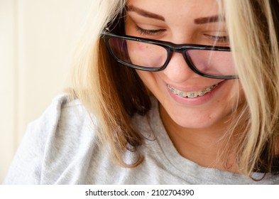 Brunette Teen Girl With Glasses. Health And Vision Care Concept With Copy Space. Beautiful Caucasian Young Girl In Braces Looks Down At Phone And Smiles.