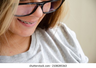 Brunette Teen Girl With Glasses. Health And Vision Care Concept With Copy Space. Beautiful Caucasian Young Girl In Braces Looks Down At Phone And Smiles.