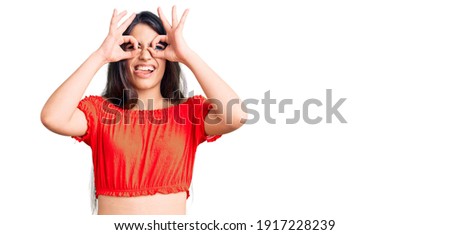 Brunette teenager girl wearing casual clothes doing ok gesture like binoculars sticking tongue out, eyes looking through fingers. crazy expression. 