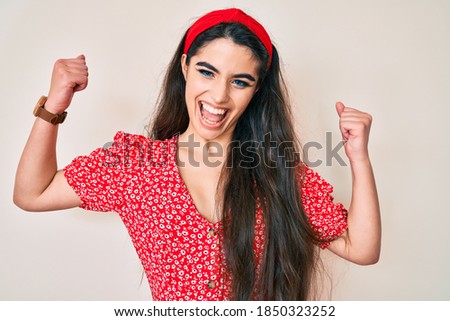 Brunette teenager girl wearing summer dress screaming proud, celebrating victory and success very excited with raised arms 