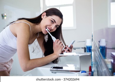 Brunette using smartphone while brushing teeth in bathroom - Powered by Shutterstock