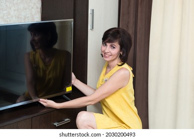 A Brunette Woman In The Apartment Installs A New Large LCD TV On The Table.