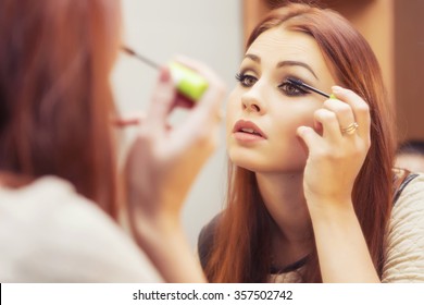 Brunette woman applying make up (paint her eyelashes) for a evening date in front of a mirror. Focus on her reflection - Shutterstock ID 357502742