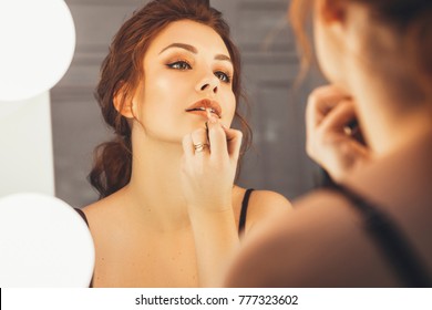 Brunette woman applying make up (paint her lips) for a evening date in front of a mirror. Focus on her reflection