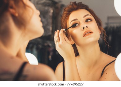 Brunette woman applying make up (paint her eyelashes) for a evening date in front of a mirror. Focus on her reflection