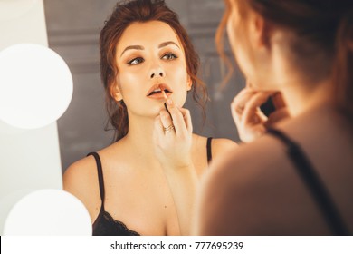 Brunette woman applying make up (paint her lips) for a evening date in front of a mirror. Focus on her reflection