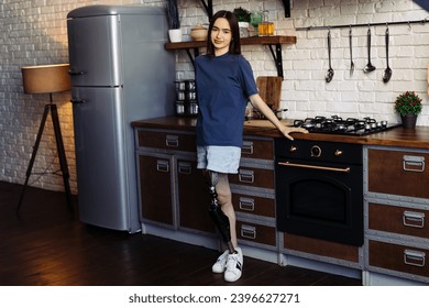 Brunette woman with artificial limb stands in kitchen with crossed arms. Female with disability exudes confidence posing for camera in cozy kitchen