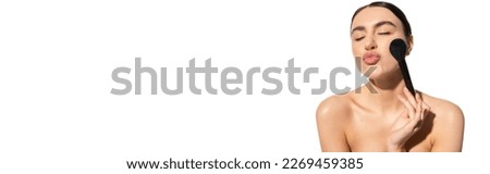 brunette woman with bare shoulders holding soft powder brush and pouting lips isolated on white, banner