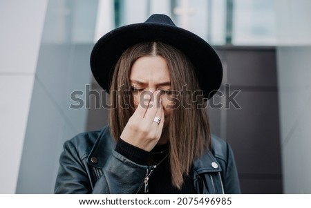 a brunette woman in a black hat suffers from a nose disease