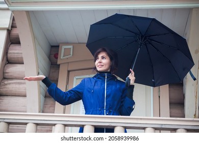 A Brunette Woman In A Blue Jacket With An Umbrella Checks With An Outstretched Hand Whether The Rain Has Stopped.