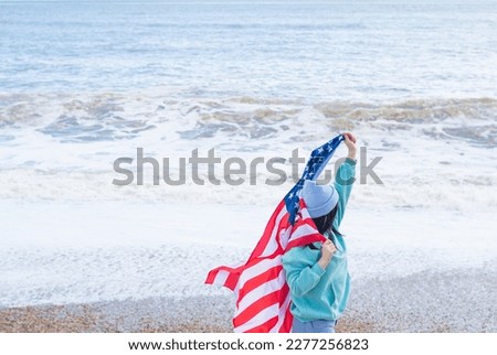 brunette woman in blue sweater and hat with american national flag near sea on the coastline
