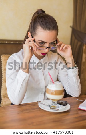 Brunette woman in business clothes and glasses sitting at the cafe drinking latte coffee.