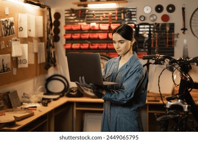 Brunette woman in casual clothes using a laptop and smiling while standing in the bicycle repair shop. Copy space - Powered by Shutterstock