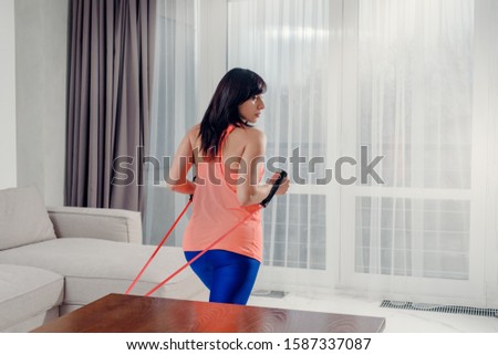 Brunette woman doing exercises with rubber band at home