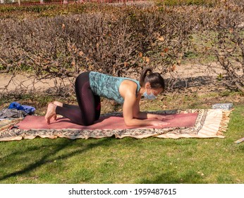 A Brunette Woman Doing Yoga Class In A Park On A Sunny Day And Wearing A Face Mask