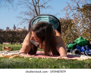 A Brunette Woman Doing Yoga Class In A Park On A Sunny Day And Wearing A Face Mask