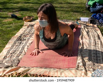 A Brunette Woman Doing Yoga Class In A Park On A Sunny Day And Wearing A Face Mask