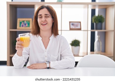 Brunette Woman Drinking Glass Of Orange Juice Winking Looking At The Camera With Sexy Expression, Cheerful And Happy Face. 