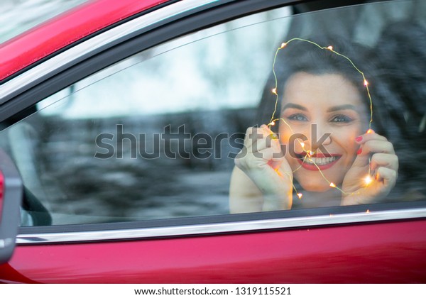 Brunette woman drive on red\
car smiling. Traveling concept. Winter holidays concept.Winter wood\
and car