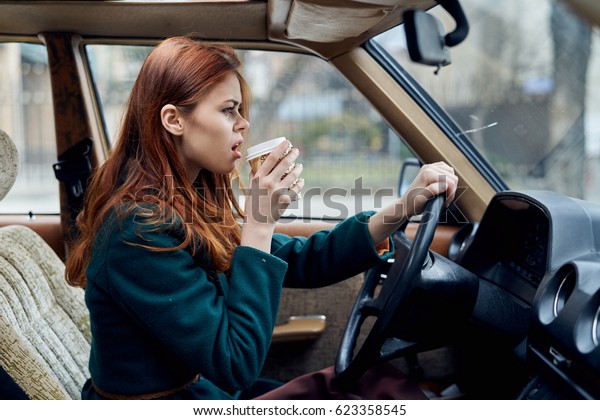 A brunette woman driving a car              \
with coffee       drink         \
