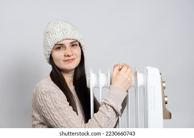 A brunette woman in a hat hugs a heater, warms up in winter, a place to text