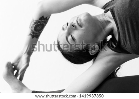 A brunette woman in her 30’s practicing yoga at home. One woman concentrated on a revolved Head-of-Knee Pose or Parivrtta Janu Sirsasana, black and white horizontal view