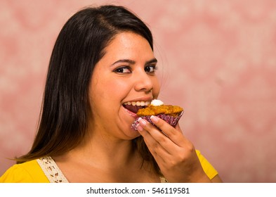 Brunette woman holding delicious brown colored muffin with cream topping, big smile and ready to take a bite, pastry concept