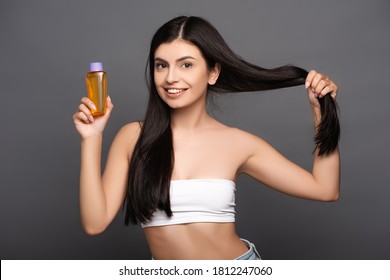 Brunette Woman Holding Hair And Oil In Bottle Isolated On Black