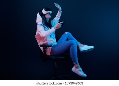 brunette woman holding joystick and gesturing while wearing virtual reality headset on blue   - Shutterstock ID 1393949603