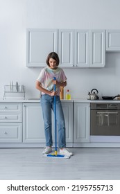 Brunette Woman Holding Mop While Cleaning Floor In Kitchen