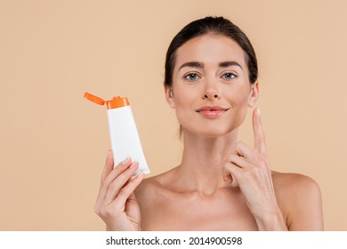 brunette woman holding sunscreen and pointing up with finger isolated on beige - Shutterstock ID 2014900598