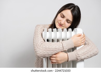 A brunette woman hugs an electric oil heater, warms up in winter.