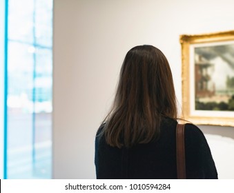 Brunette Woman Looking At Artwork In Museum. Rear View.