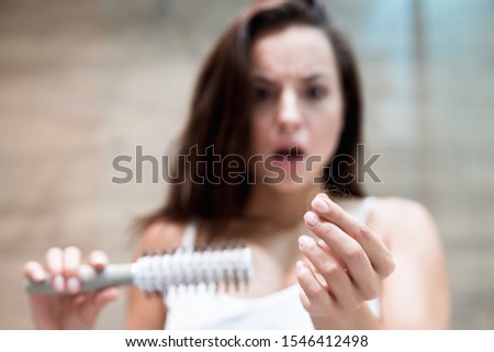 brunette woman looking frightened when sees a lot of fallen hair on the brush hair loss problem