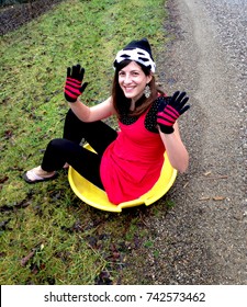 A Brunette Woman Prepares To Descend A Slope On A Sled On Christmas Day, Despite There Being No Snow On The Ground. 