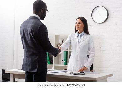 brunette woman shaking hands with african american patient wearing suit