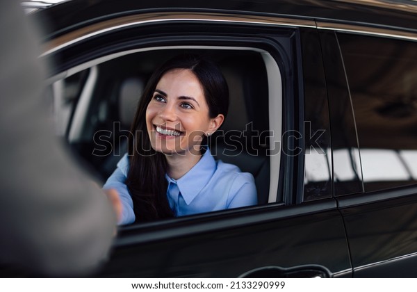 Brunette\
woman, shaking hands with someone, from her\
car.