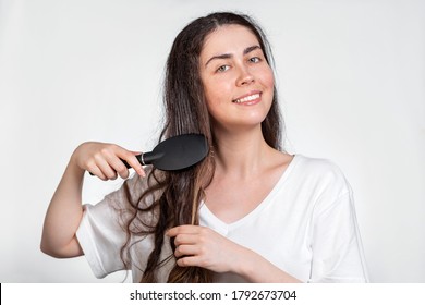 The Brunette Woman Smiles And Combs Her Hair. White Background. Copy Space. Hair Care Concept
