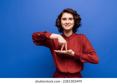 brunette woman smiling and showing gesture meaning stand on sign language isolated on blue - Shutterstock ID 2281303499