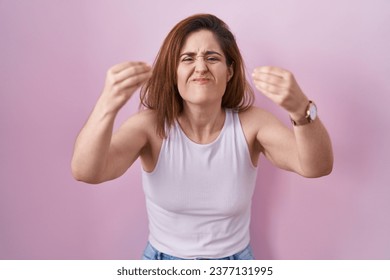Brunette woman standing over pink background angry and mad raising fists frustrated and furious while shouting with anger. rage and aggressive concept.  - Shutterstock ID 2377131995
