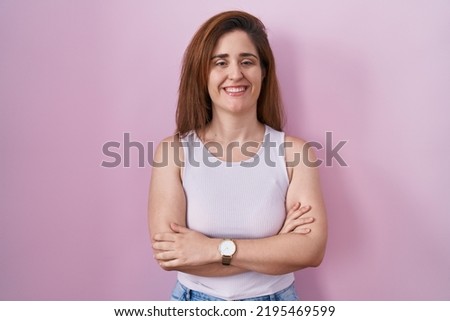 Brunette woman standing over pink background happy face smiling with crossed arms looking at the camera. positive person. 