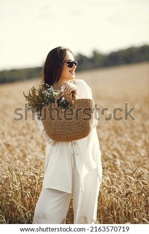 Brunette woman with a straw bag walking in wheat field