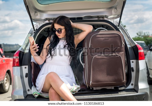 Brunette woman\
with suitcase and phone in car\
trunk