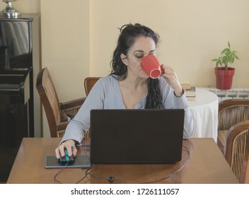 Brunette Woman Telecommuting At Home Drinking From A Mug In Front Of Her Laptop