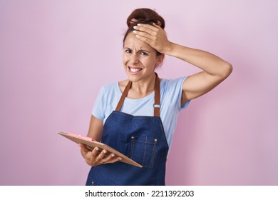 Brunette Woman Wearing Professional Waitress Apron Holding Clipboard Stressed And Frustrated With Hand On Head, Surprised And Angry Face 